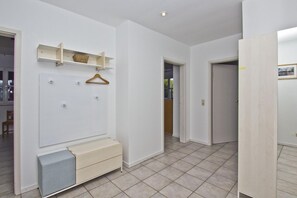Ein Flur mit weißer Wand, einer Holzbank, einem Hängegestell und einer Tür zu einem anderen Raum.