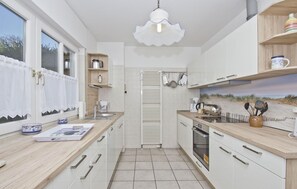 Eine moderne Küche mit weißen Schränken, einer Holz Arbeitsplatte, einem eingebauten Ofen und einem Fenster mit weißen Vorhängen.