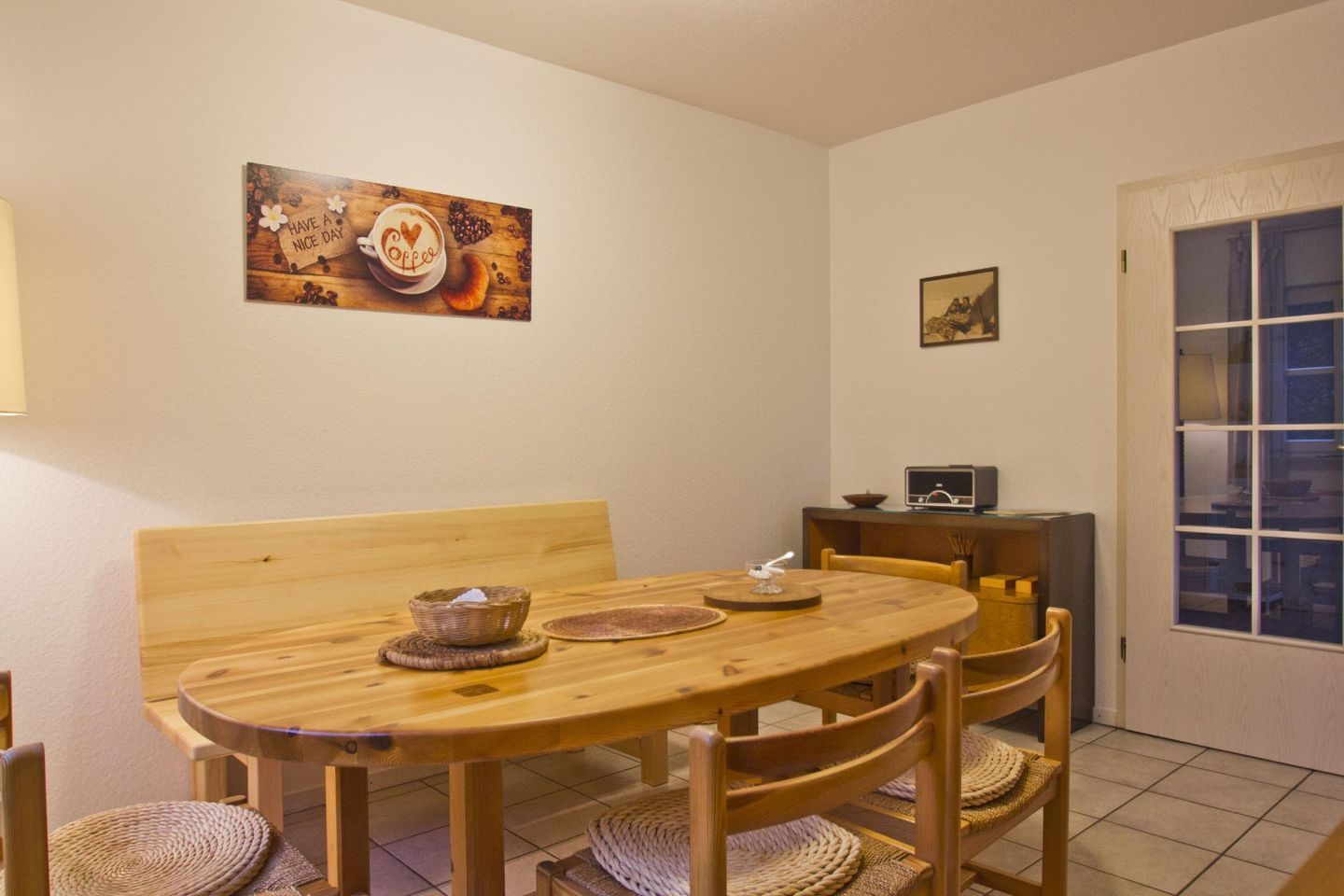 A cozy dining area with a wooden table and chairs, a bench, a small basket, and a decorative coffee cup on the wall.