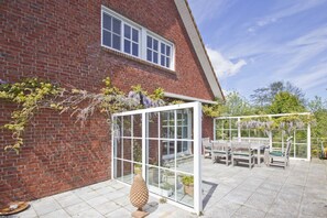 A brick house with a glass conservatory, a patio with a table and chairs, and a decorative stone sculpture. - Vacation apartment close to the beach with a beautiful garden - Ferienhaus Gisela - Holiday home (Putbus)
