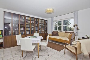 A living room with a dining table, chairs, a sofa, a bookshelf, and a window.