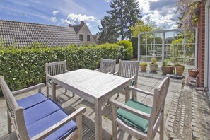 A patio with a wooden table and chairs, surrounded by potted plants and a glass enclosure. - Vacation apartment close to the beach with a beautiful garden - Ferienhaus Gisela - Holiday home (Putbus)