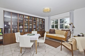 Ein Wohnzimmer mit Esstisch, Stühlen, einer Couch, einem Bücherregal und einem Fenster.