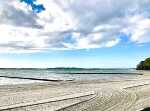 A beach with a wide sandy shore and a calm sea under a partly cloudy sky.