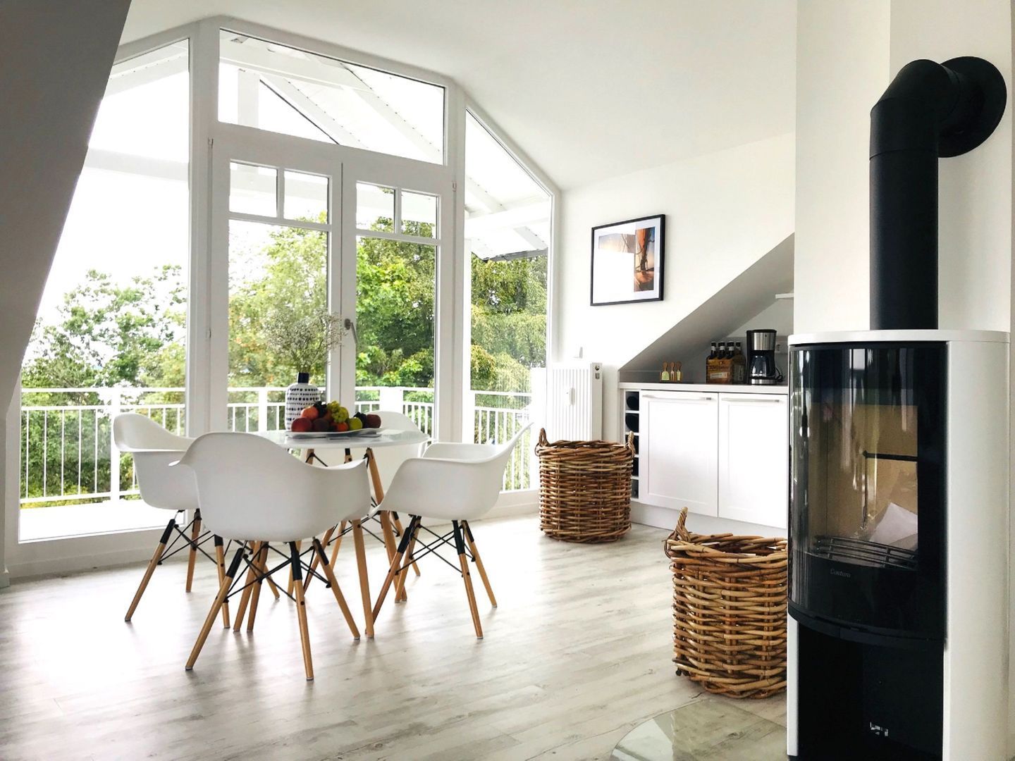 A modern kitchen with a large window, white cabinets, a black stove, and a dining area with white chairs.