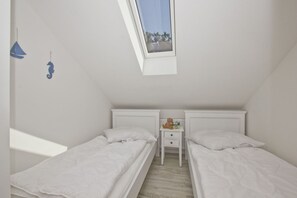 A bedroom with two single beds, a small bedside table with a teddy bear, and a window with a view of trees. - Modern vacation apartment with a balcony and ocean view - Ferienresidenz Zwei Bodden, Vacation Rental 1-5 (Lietzow)
