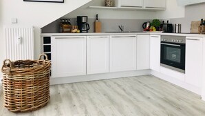 A modern kitchen with white cabinets, a built-in oven, and a coffee maker. - Modern vacation apartment with balcony, sea view - Ferienresidenz Zwei BoddenFeWo 1-5 (Lietzow)