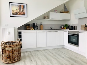 A modern kitchen with white cabinets, a built-in oven, and a coffee maker. - Modern vacation apartment with a balcony and ocean view - Ferienresidenz Zwei Bodden, Vacation Rental 1-5 (Lietzow)