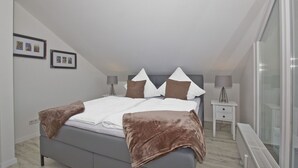 A bedroom with a bed, bedside tables, and a radiator. - Modern vacation apartment with balcony, sea view - Ferienresidenz Zwei BoddenFeWo 1-5 (Lietzow)
