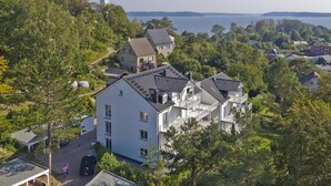 A multi-story building with a flat roof, surrounded by trees and a body of water in the background. - Modern vacation apartment with balcony, sea view - Ferienresidenz Zwei BoddenFeWo 1-5 (Lietzow)