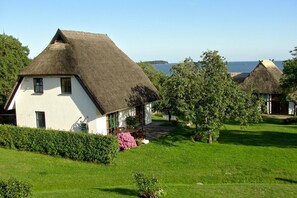 A traditional house with a thatched roof, surrounded by lush greenery and a clear view of the sea. - Gutshof Ostseeblick - A Seaside Paradise, Private Swimming Area, Beach Chair (Putbus)