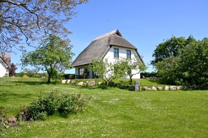 A traditional house with a thatched roof, surrounded by a well-maintained lawn and a stone wall. - Gutshof Ostseeblick - beachfront idyll by the sea, private bathing area, beach chair (Putbus)