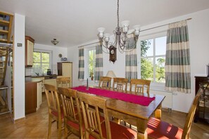 Ein Essbereich mit einem Holztisch und Stühlen, einer Kronleuchter und Blick ins Freie durch große Fenster.