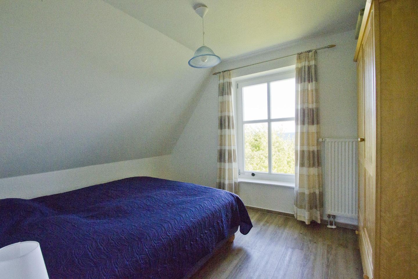 A bedroom with a bed, a window with curtains, a radiator, and a door.
