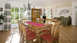 Un comedor con una mesa y sillas de madera, una araña y vistas al exterior.