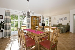 Un comedor con una mesa y sillas de madera, una araña y vistas al exterior.