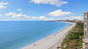 Ein Küstenstrand mit weitem Sandstreifen, blauem, klarem Meer und einigen Gebäuden entlang der Küste.