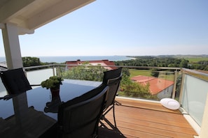 En balkon med et glasbord og stole, der ud til et naturskønt landskab med bygninger og vand.