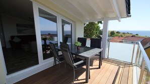 Uma varanda com mesa e cadeiras, um vaso de planta e vista para o mar.