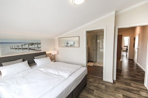 Et hotelværelse med en stor seng, et maleri af en strand, et spejl og et bruseområde.