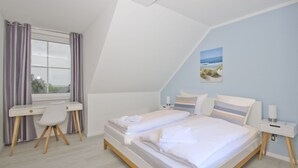 A bedroom with a bed, a desk, and a chair. - Vacation apartment with sea view and garden use - Haus Inselwind FeWo MEERduft - (Gager)