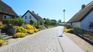A cobblestone street lined with traditional houses, a clear sky, and a well-maintained flower bed. - Vacation apartment with sea view and garden use - Haus Inselwind FeWo MEERduft - (Gager)