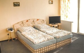 Ein Doppelbett mit blumigem Bettzeug, ein Fernseher auf einem Schrank und ein kleiner Tisch mit einem Radio.