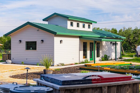 A single-story house with a green roof and white siding, featuring a front porch and a small attached garage.