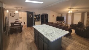 A modern kitchen with a central island, a dining area with chairs, a living room with a sofa and TV, and a hallway leading to a bedroom. - The DW - Spacious and Cozy (Columbia)