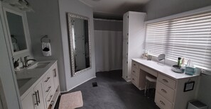 Een badkamer met een witte wastafel, een grote spiegel en een raam met zonwering.