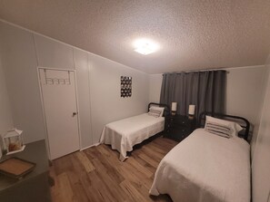 Een slaapkamer met twee eenpersoonsbedden, een kledingkast, een klein tafeltje en een plafondlamp.