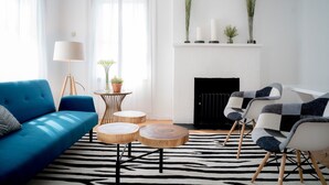 A modern living room with a blue sofa, a patterned armchair, a round wooden coffee table, a floor lamp, and a fireplace with decorative items. - 3 Bedroom 2 Bath (Poway)