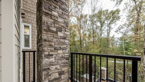 A balcony with a stone wall, black railing, and a view of trees. - 3 Bedroom 2 Bath (Poway)