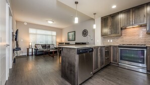 A modern kitchen with a central island, stainless steel appliances, and a dining area with a sofa and coffee table. - 3 Bedroom 2 Bath (Poway)