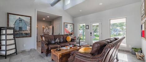 A spacious living room with a high ceiling, a fireplace, and a large window offering a view of the outdoors.