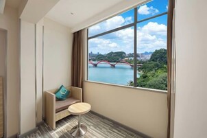 Una habitación con un ventanal grande, una pequeña mesa redonda, un banco con cojín y vista a un puente sobre un río.