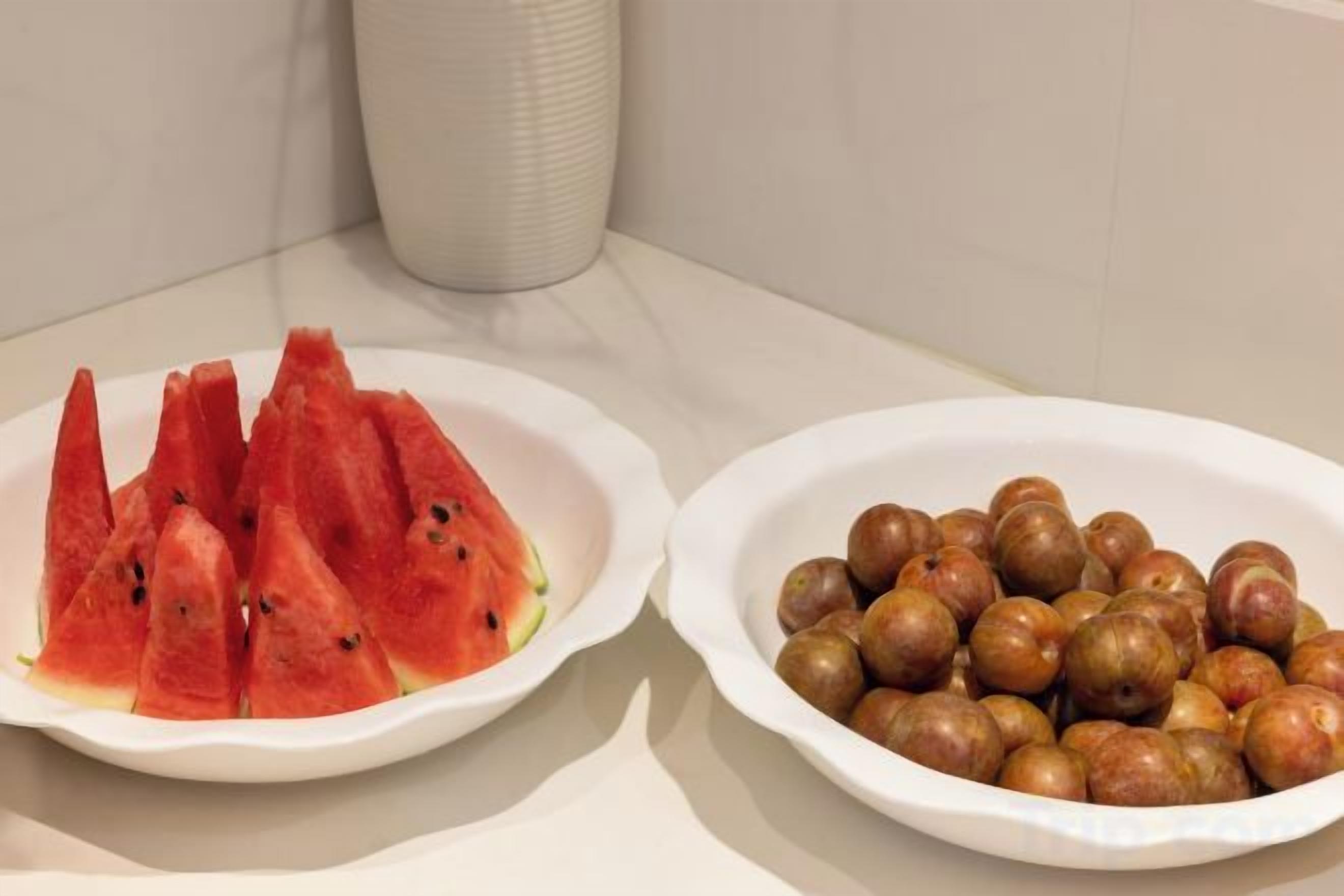 Two white ceramic dishes, one containing sliced watermelon and the other containing nuts, on a kitchen counter.