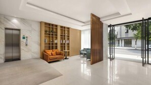 Un vestíbulo moderno con una recepción de mármol, una estantería de madera, un sofá y una puerta de cristal que da al exterior.