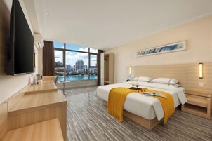 Habitación de hotel moderna con una cama grande, un escritorio, un televisor y vistas a la ciudad.
