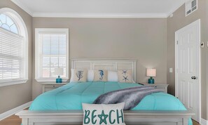 A bedroom with a bed, a nightstand, a lamp, a window with blinds, and a door.