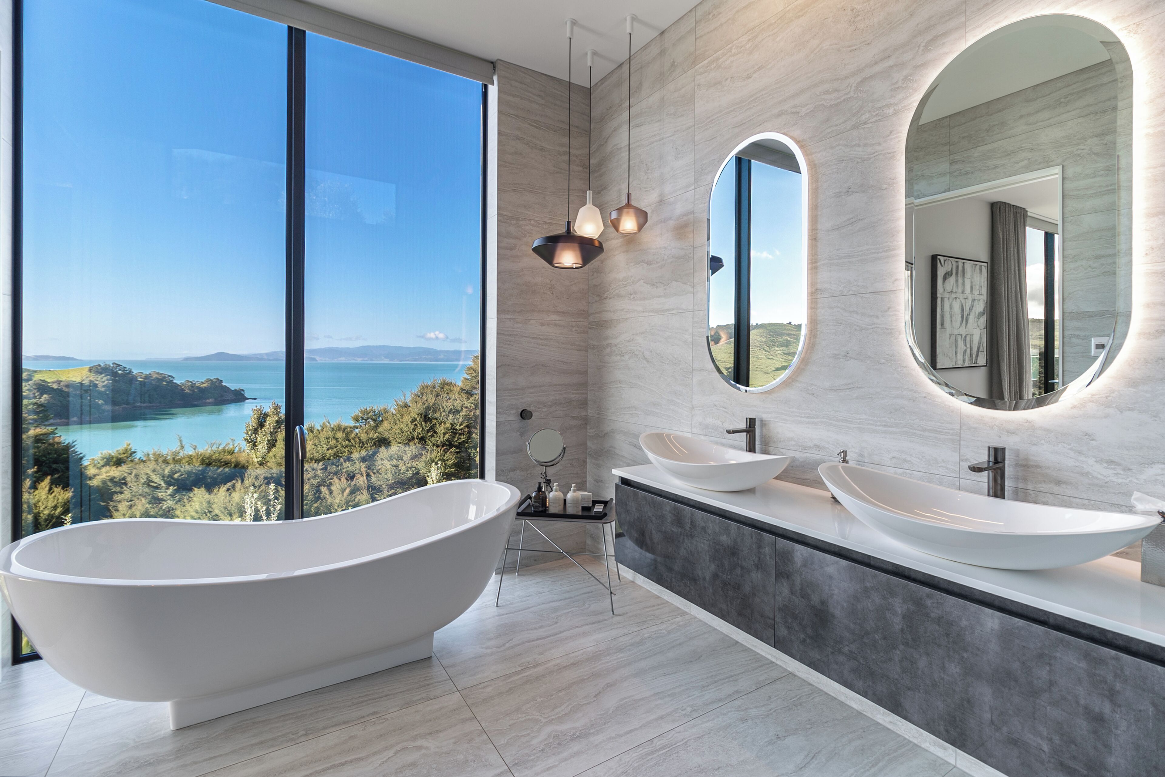 Un baño moderno con una bañera independiente, dos lavamanos y amplias ventanas con vistas panorámicas.