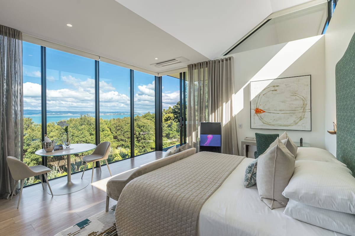 Ein modernes Schlafzimmer mit einem großen Bett, einem kleinen Tisch und Stühlen. Es verfügt über ein großes Fenster mit Blick ins Freie.