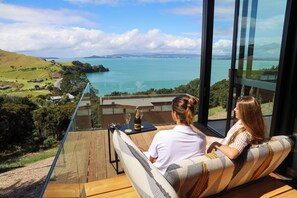 A couple seated on a balcony overlooking a scenic view of a lake and distant mountains. - Omana (Waiheke Island)