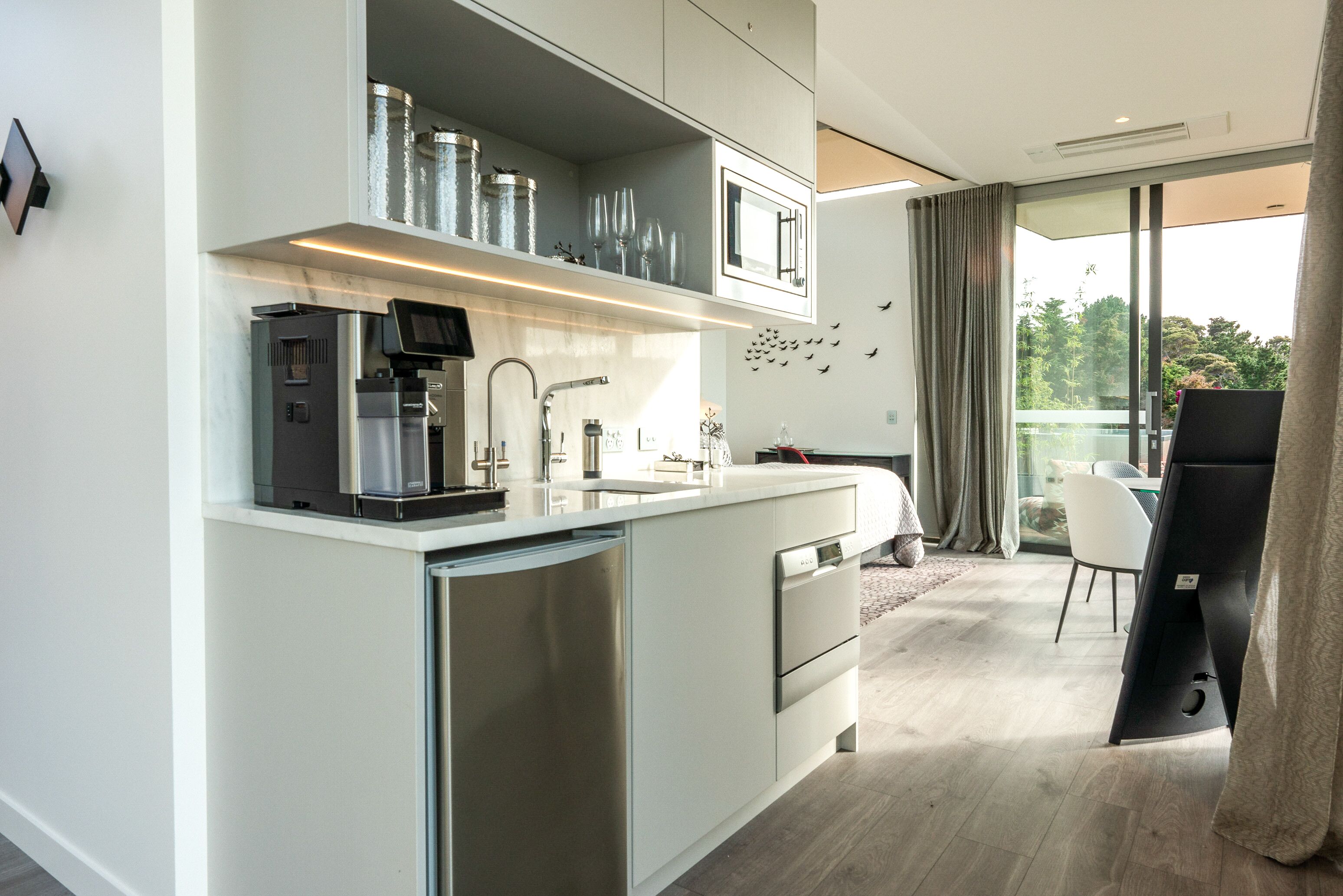 Eine moderne Küche mit integrierter Kaffeemaschine, Edelstahlgeräten und einem großen Fenster mit Blick auf einen Balkon.