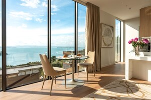 Ein modernes Zimmer mit einem großen Fensterglas, einem runden Esstisch, zwei Stühlen und Meerblick.