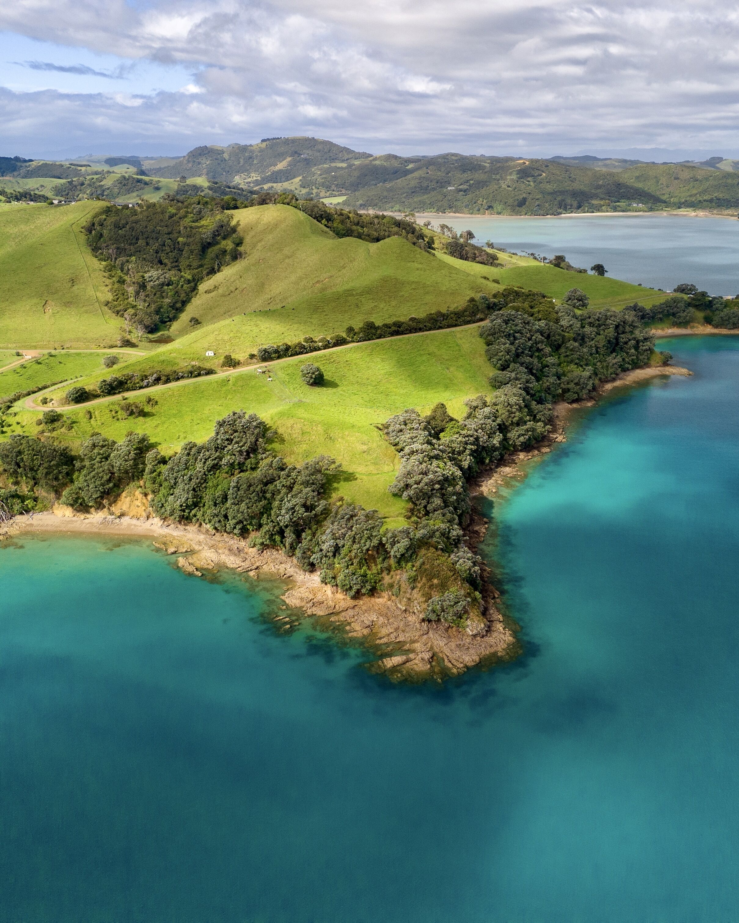 A coastal landscape with rolling hills, a beach, and clear turquoise waters.