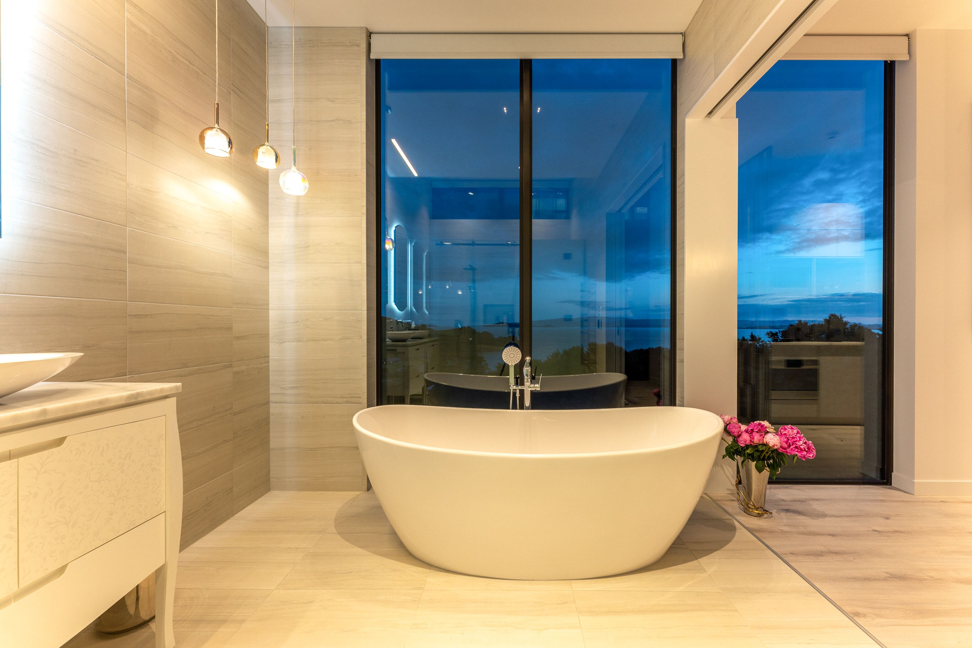 A modern bathroom with a freestanding bathtub, a vanity with a bowl sink, and a large window offering a view of the cityscape.