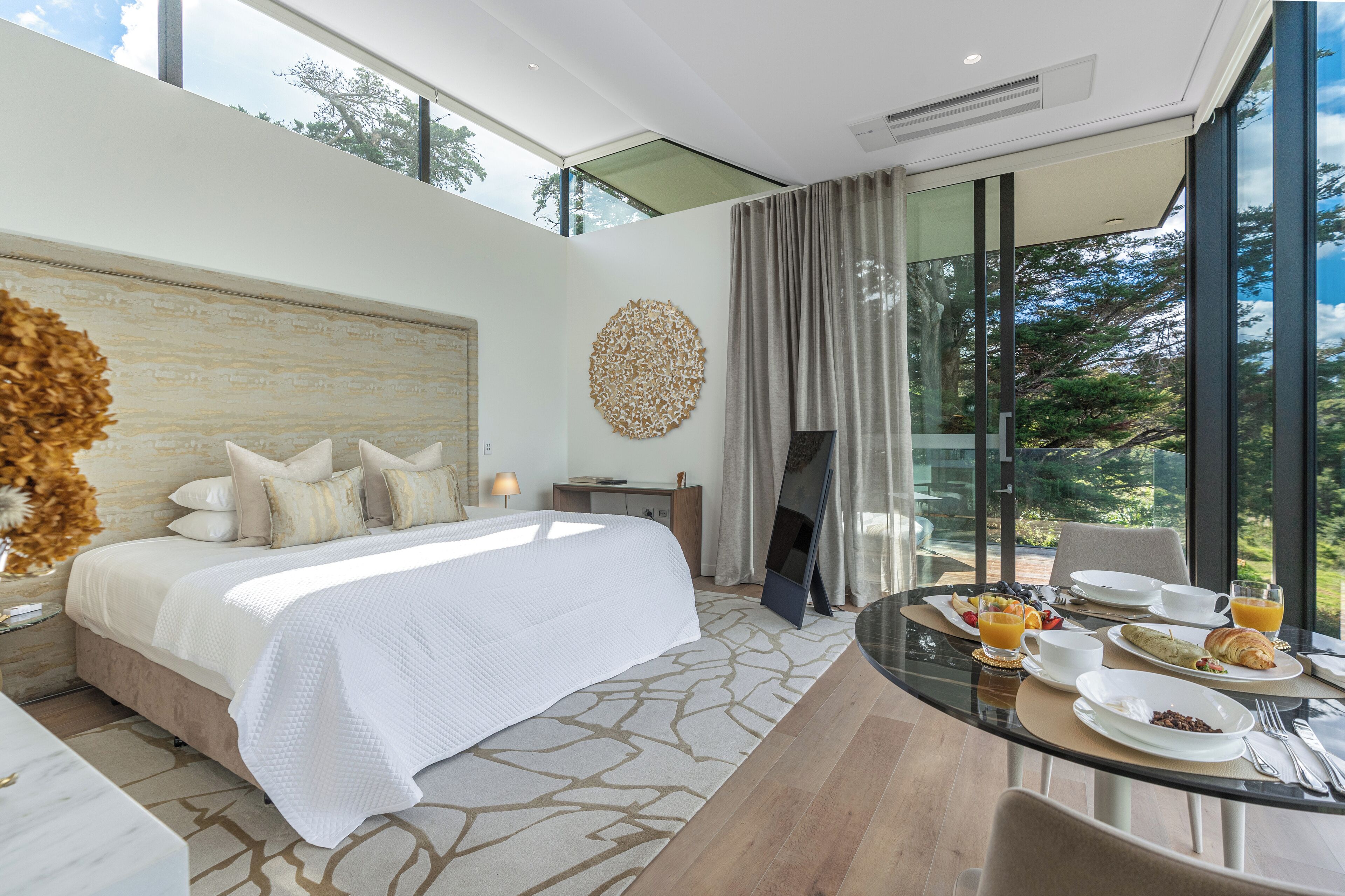 Un hotel moderno con una cama grande, una mesa de comedor con desayuno, y vistas al exterior.