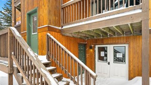 Ein Holzhaus mit einer grünen Tür, einer Treppe mit Holzgeländer und verschneitem Grund.