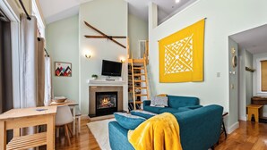 Ein gemütliches Wohnzimmer mit einem türkisblauen Sofa, einem Kamin, einem Fernseher und einem gelben Wandbild.